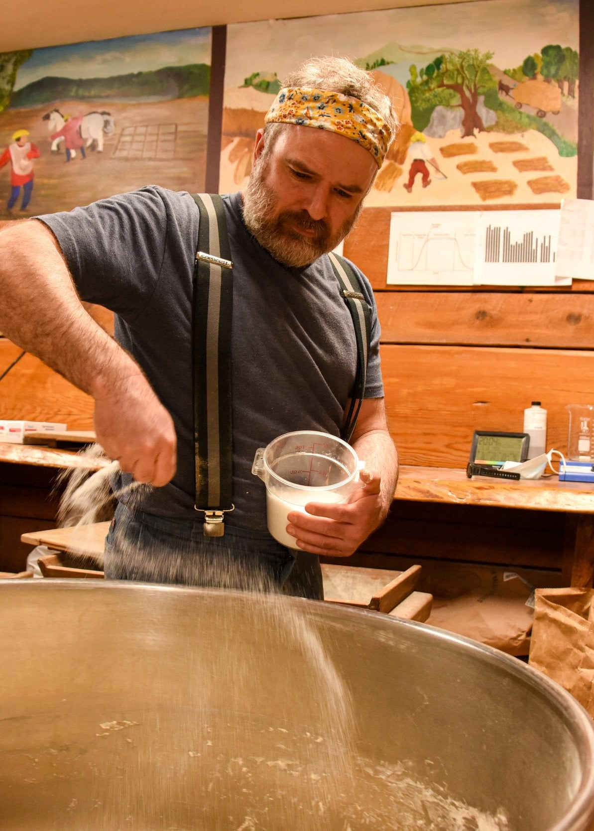 A person is stirring ingredients in a large metal bowl, preparing to make bread.